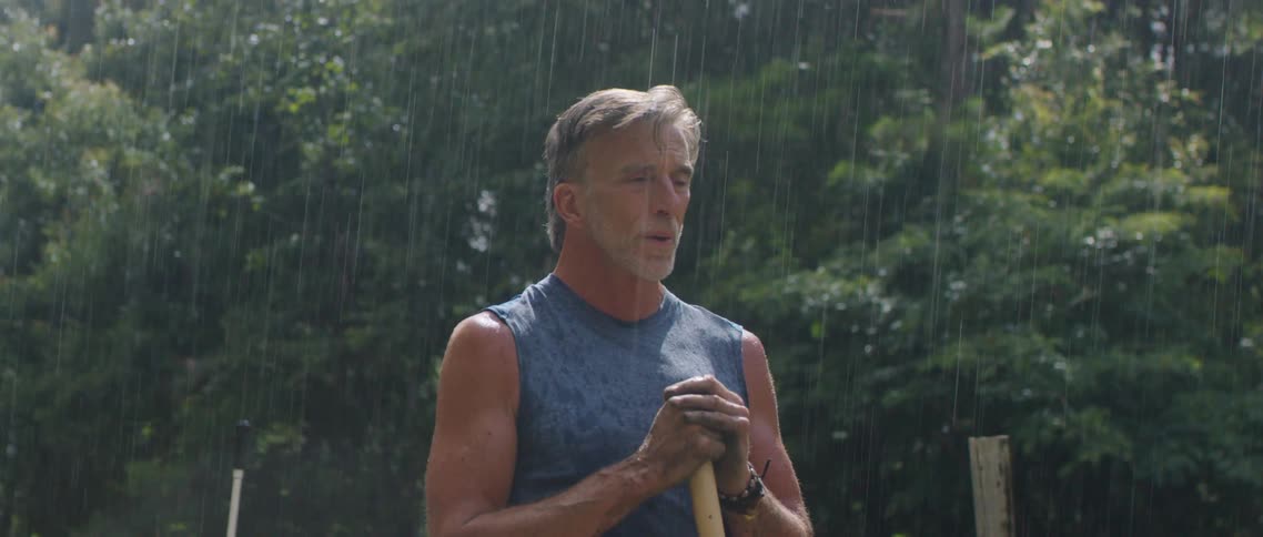 Man standing in a garden under the rain with a shovel in his hands