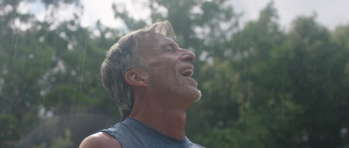 A man stands outside in the rain holding his hands together and looks up at the sky