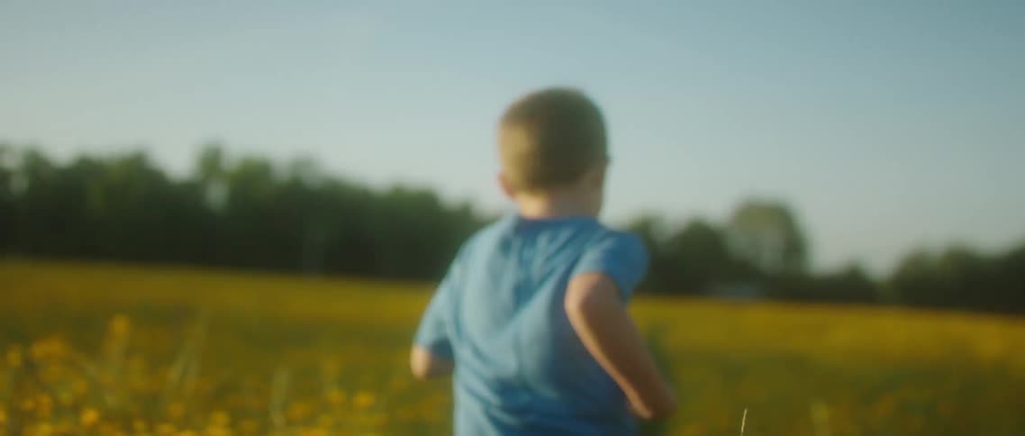 A boy in a blue t shirt runs through a field filled with knee high grass and yellow flowers