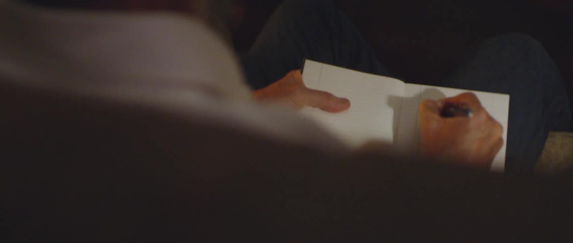 A man sits in front of a fireplace writing in a notebook