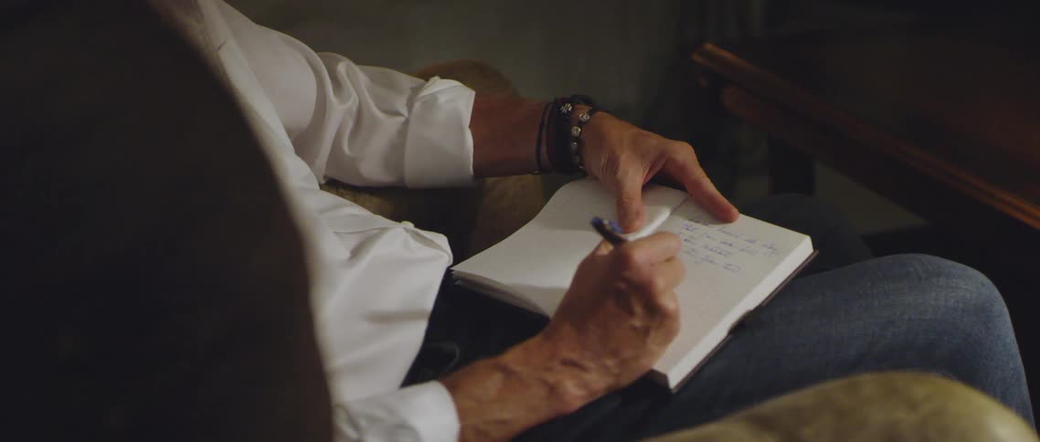A man sitting in a chair writes in a notebook