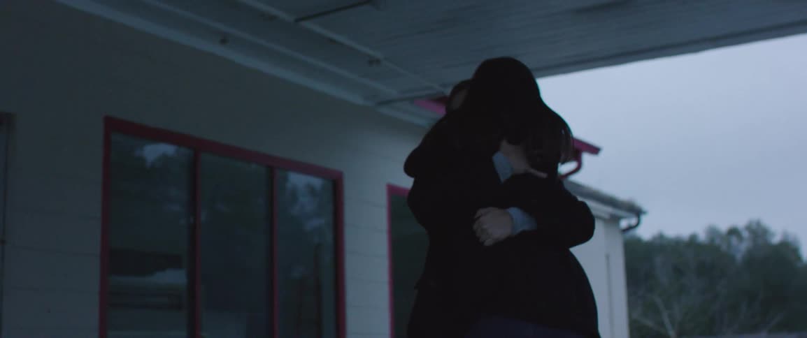 A man and woman embrace outside of a small building on a cloudy day