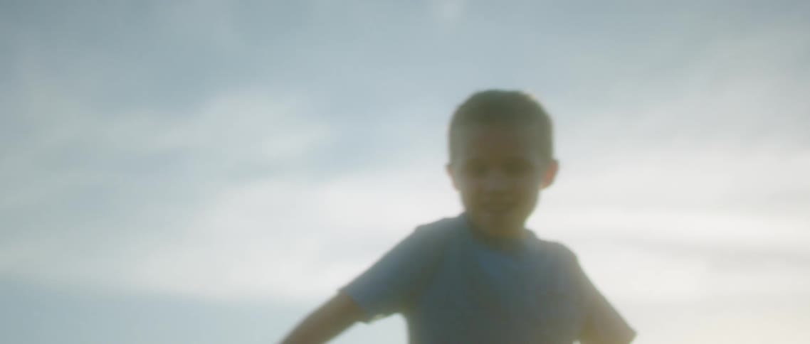 A boy wearing a blue t shirt spins around outside playing in a field with flowers