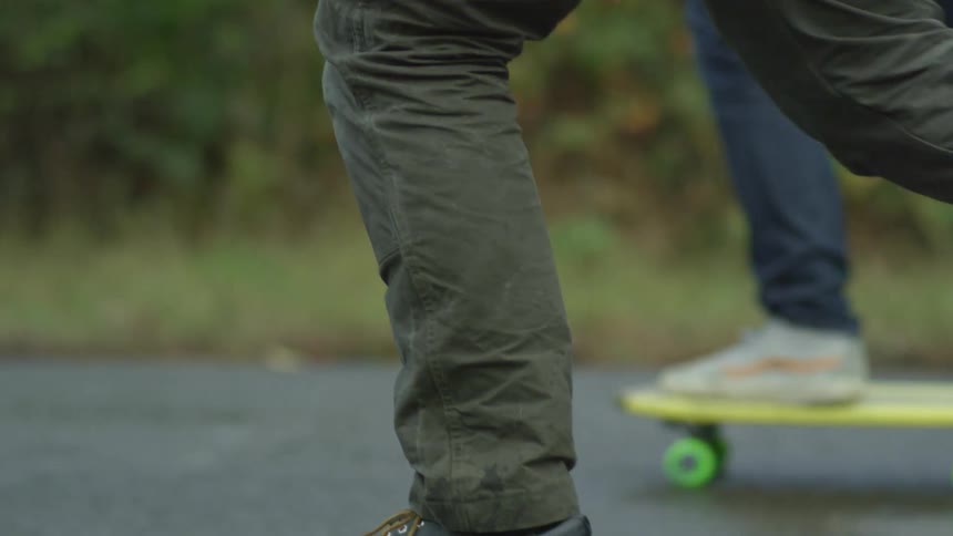 Two men carrying skateboards walk and then set them down and step on them and skateboard down a road