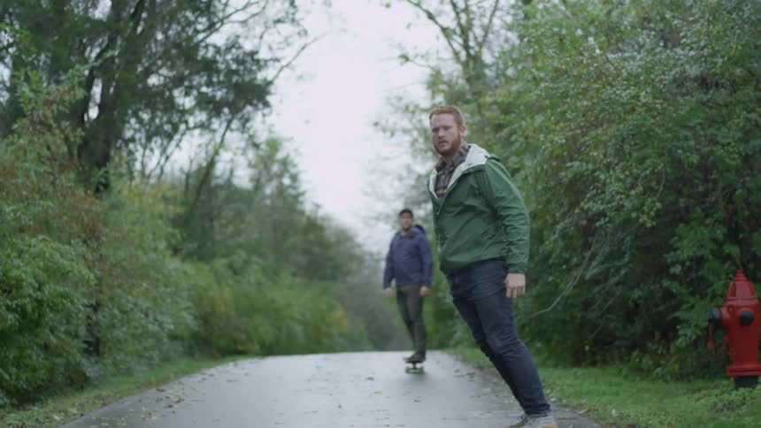 Two men skateboarding down a road next to a wooded area