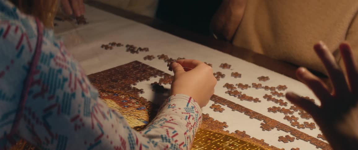 A young girl sits at a table with others and works on a puzzle