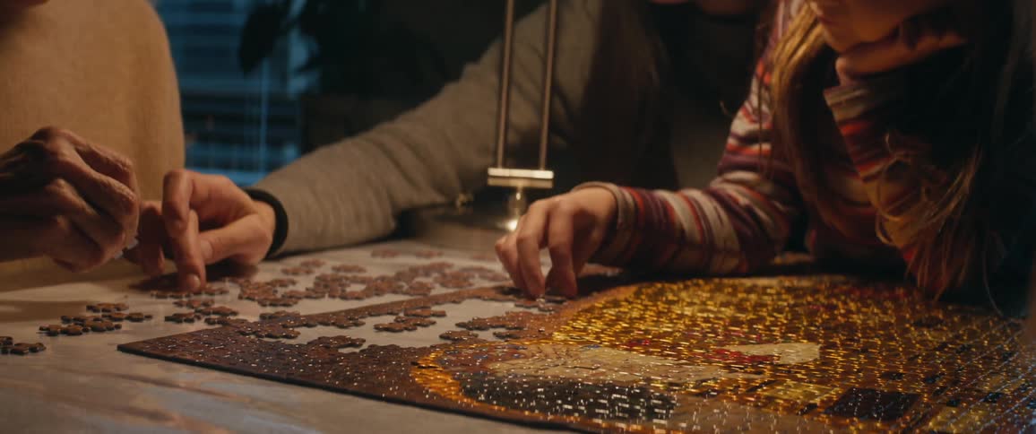 A young girl sits on her mothers lap as they and other family members work on a puzzle together