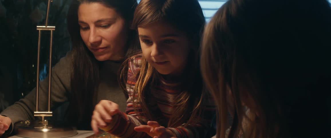 A girl sits on a womans lap as they sit at a table laughing with another girl