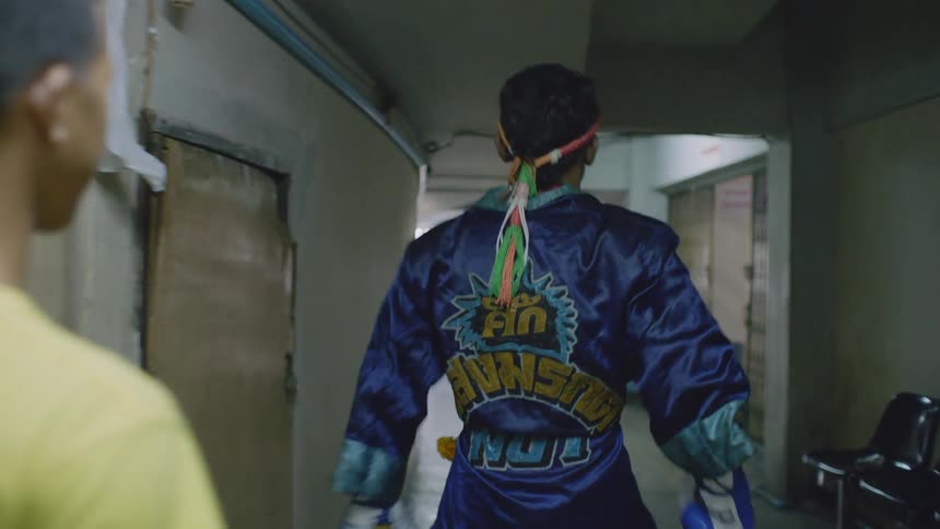 A muay thai fighter stretches and shadow boxes while walking through a corridor on his way to his match