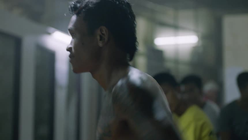 A man wearing boxing gloves stretches and warms up while standing in front of a group of men