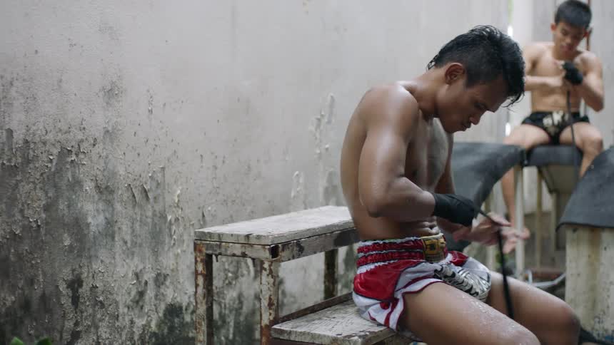 Young strong barechested fit muay thai fighter gearing up for combat in a gym