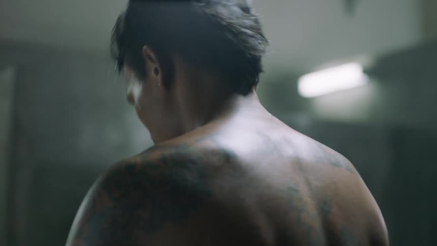 Boxer with tattooed back and arms wearing yellow gloves warming up, stretches and flexes