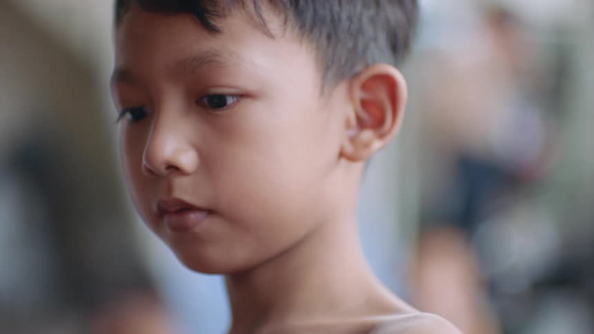 A boy stands outside with people behind him