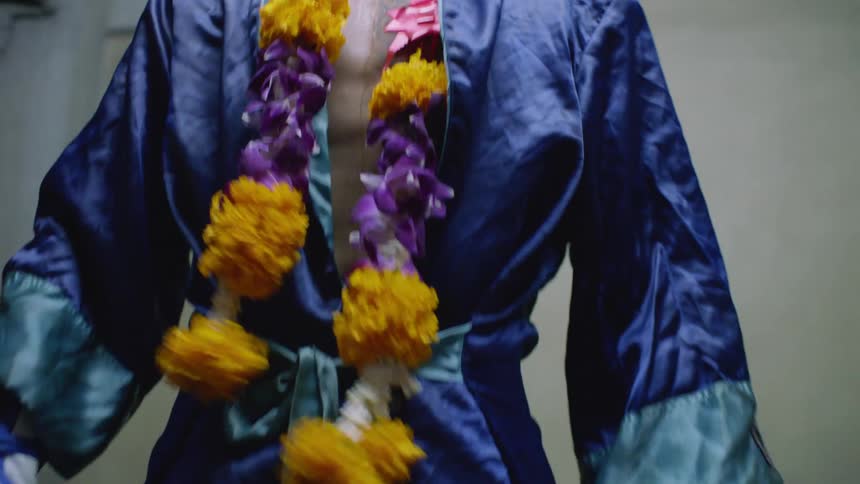 A man wearing a robe and boxing gloves with a decorative garment around his neck pants while standing up in a room