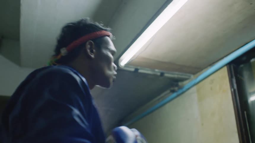A man wears a blue satin robe and is practicing boxing while standing indoors