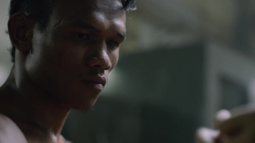Coach tying boxing gloves on a strong muscular shirtless young muai thai boxer