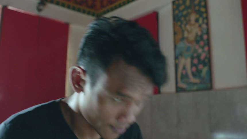 A young man repeatedly bows as he prays in a building during the day
