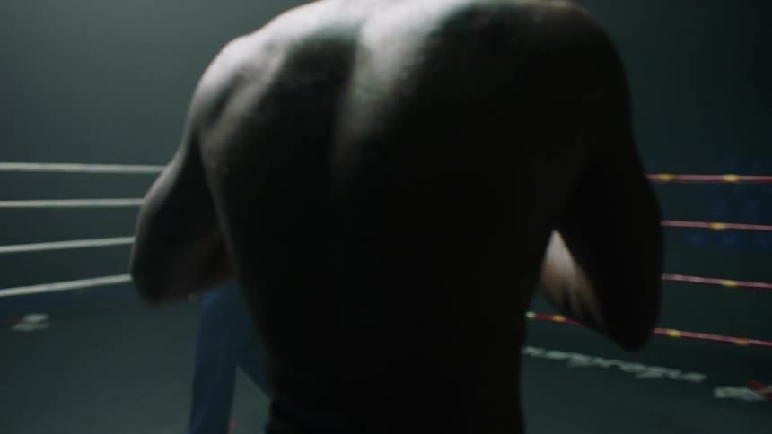 A pair of men exchange punches and kicks as they fight in a boxing ring while a referee circles them in a dimly lit arena