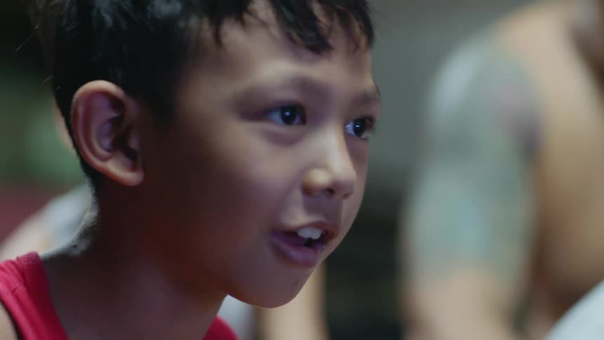 A boy imitates punches and kicks as he sits in a crowd watching a professional fight