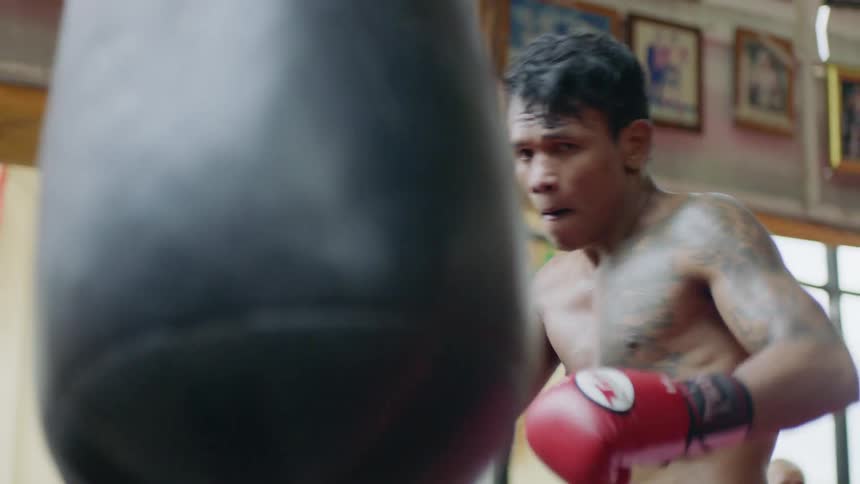A boxer throws powerful punches at a punching bag in a gym during the day