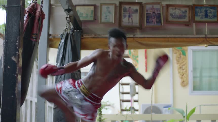 A man strikes a hanging punching bag with his punches elbows and kicks while training during the day