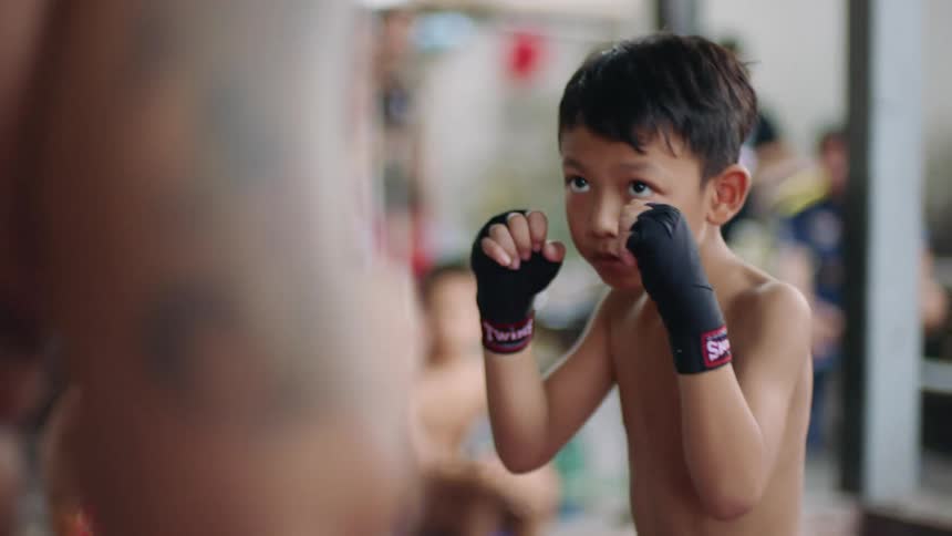 A young boy practices boxing as he throws strikes at his coach