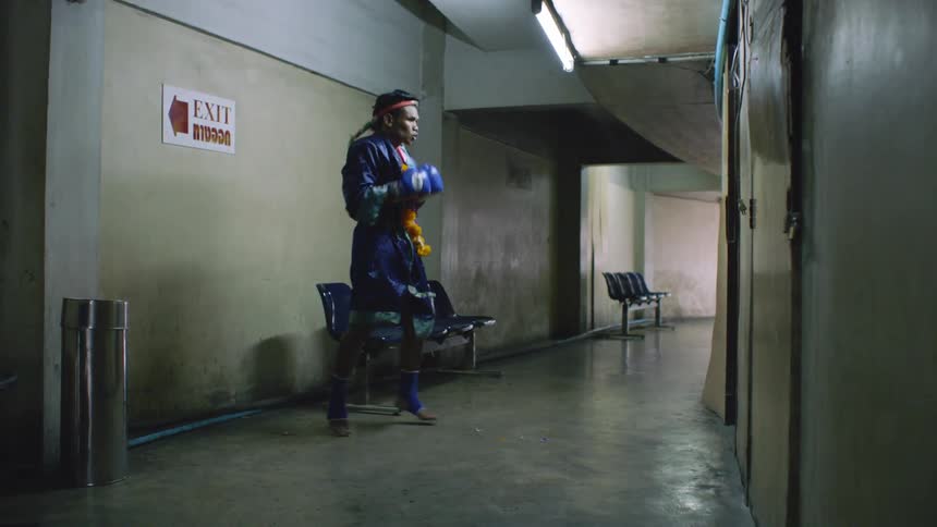 A muay thai fighter wearing a robe shadow boxes in the corridor of a building