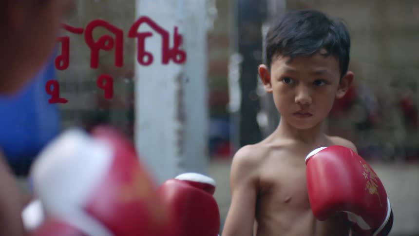 A boy wearing boxing gloves poses light a boxer in front of a mirror in a gym