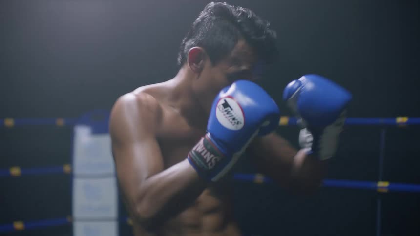 Two men one in red one in blue fight in a kickboxing style in a ring with blue ropes