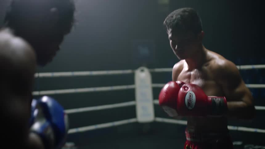 A pair of professional fighters exchange punches in a boxing ring in a dimly lit sports arena