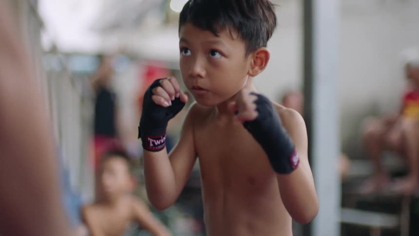 Boy studies boxing from male instructor as others watch