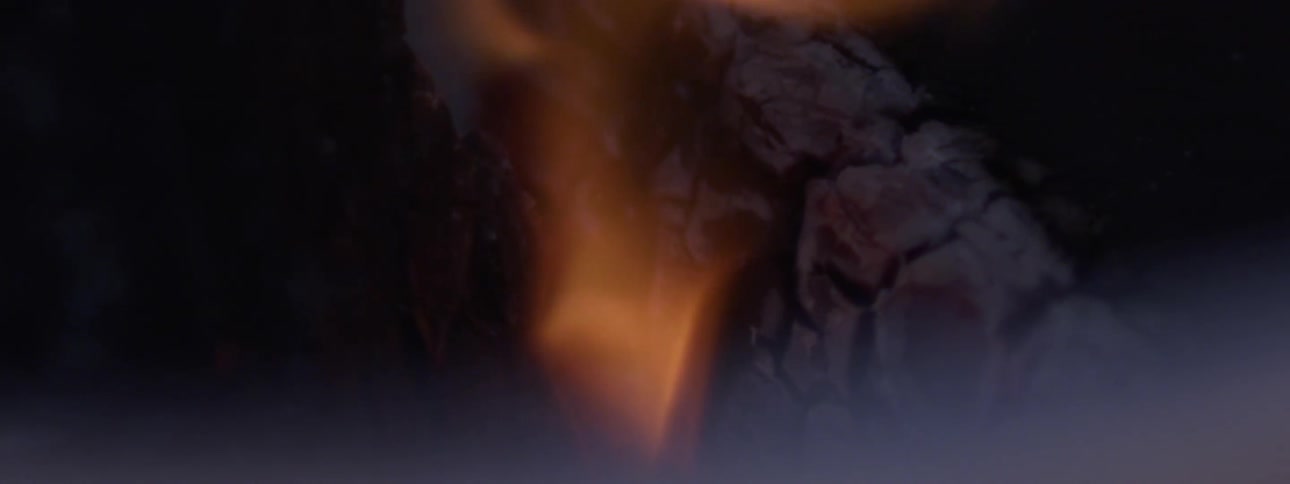 Flame burns over charred wood in darkness