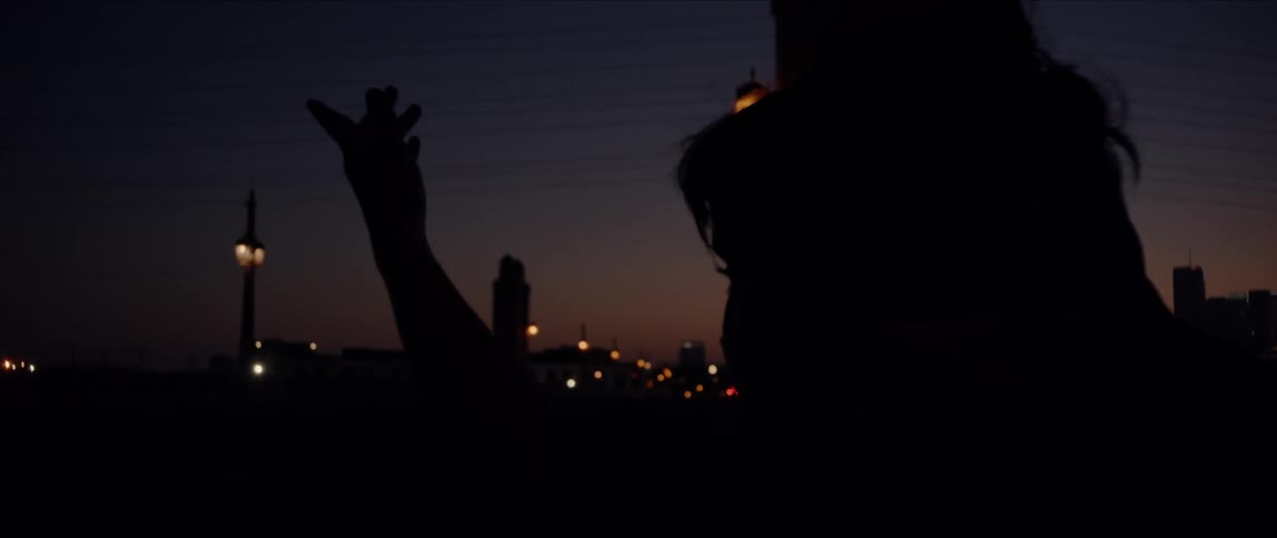 Person spins past camera in front of street lamps and a city with lights on