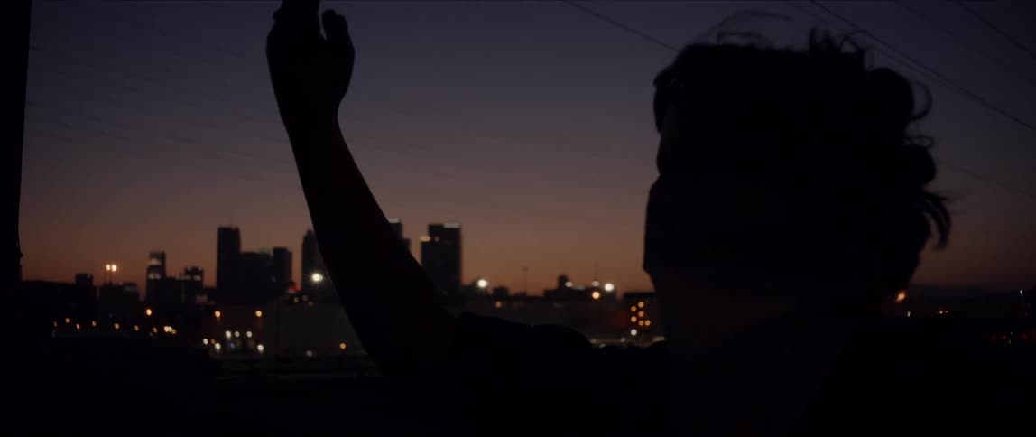 Silhouette of female dancer moves against distant backdrop of city skyline at night