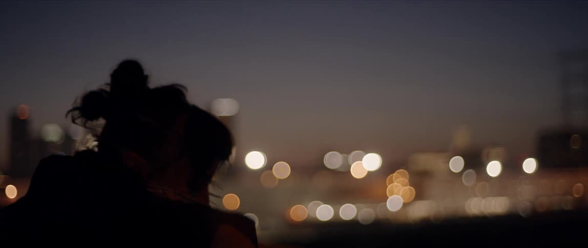 A young woman with a bandana around her face dances outdoors in a metropolis at night