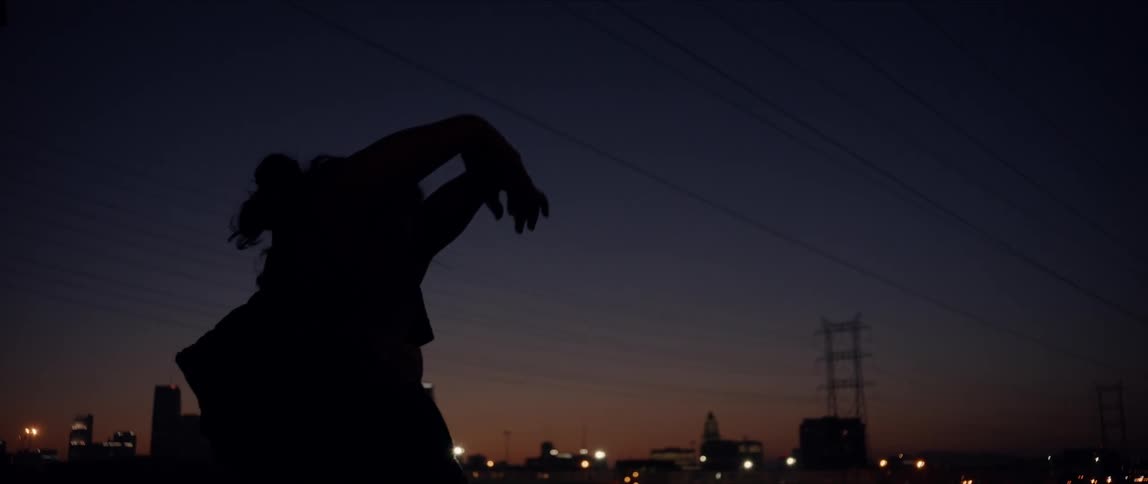 Womans silhouette spins and turns at night with city skyline on horizon