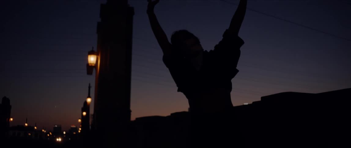 Young woman performing a dance pose on a bridge at evening
