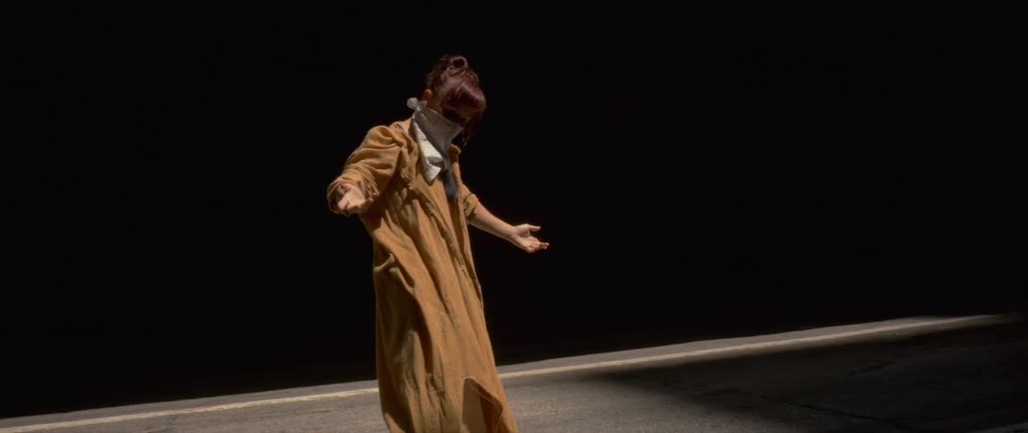 Young woman wearing a yellow robe and a face mask dancing at night outdoors