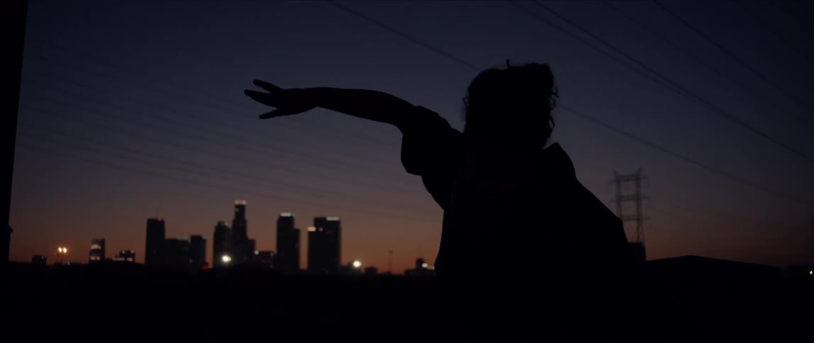 A woman moves her arms and does a body roll as she dances outside in front of a city