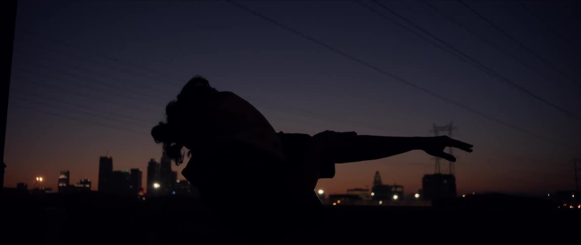 A woman dancing outside at night in front of the city skyline