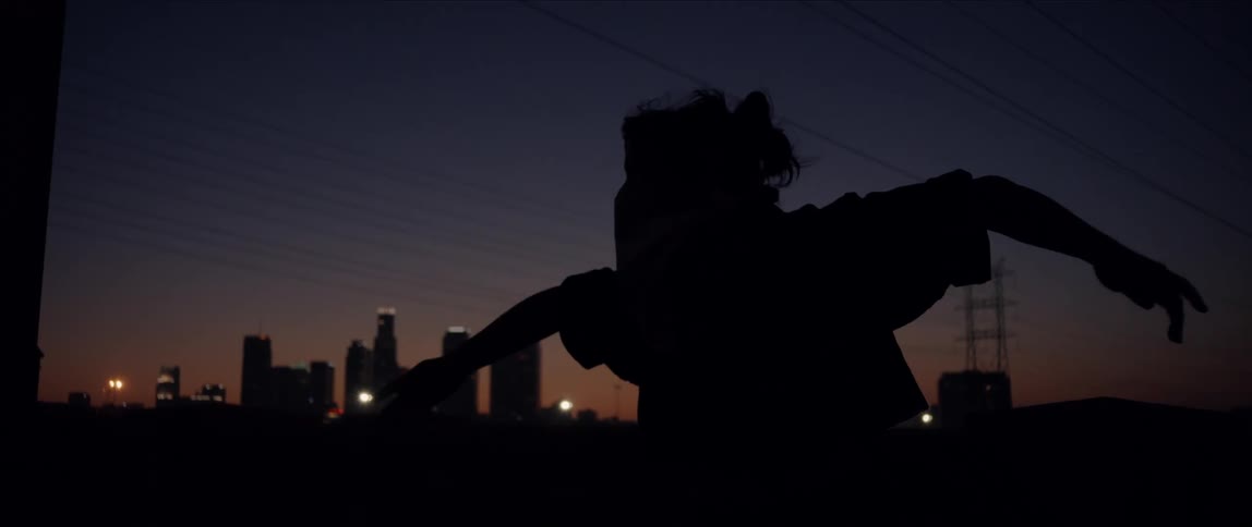 Dancers silhouette moves against night sky with city skyline in background