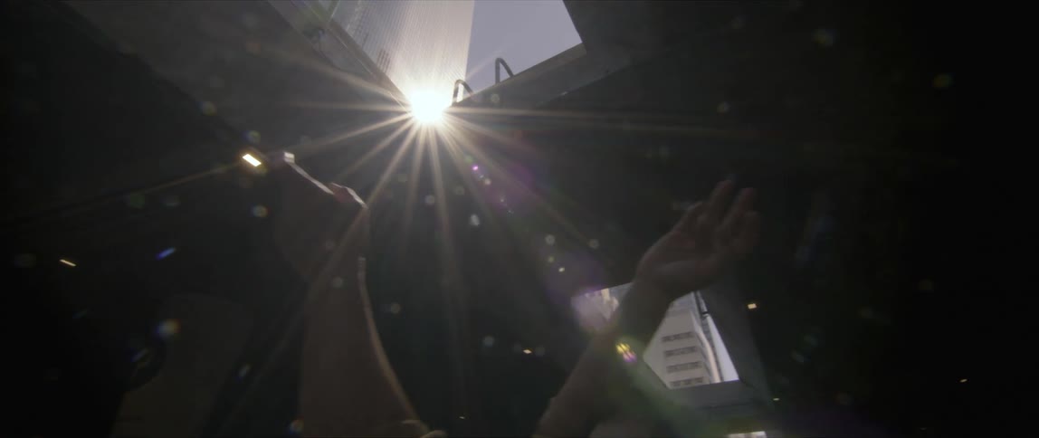 Woman wearing bandana mask dances under bridge in sun shining from sky past skyscraper