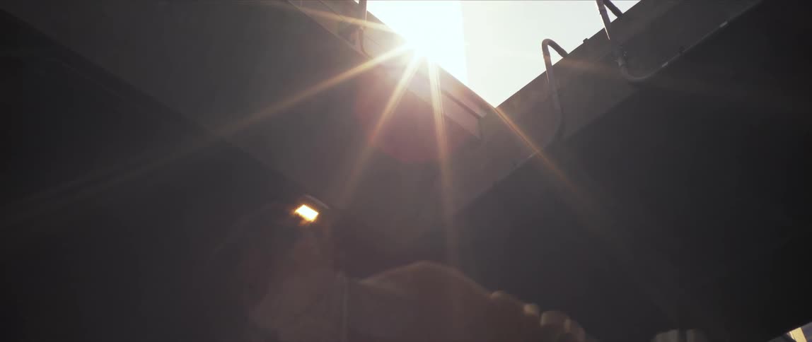 Sunlight shines through a gap in a building onto a dancing young woman wearing a bandana over her lower face