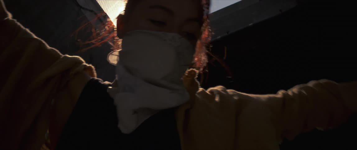 A female wearing a scarf over her face is dancing in front of buildings