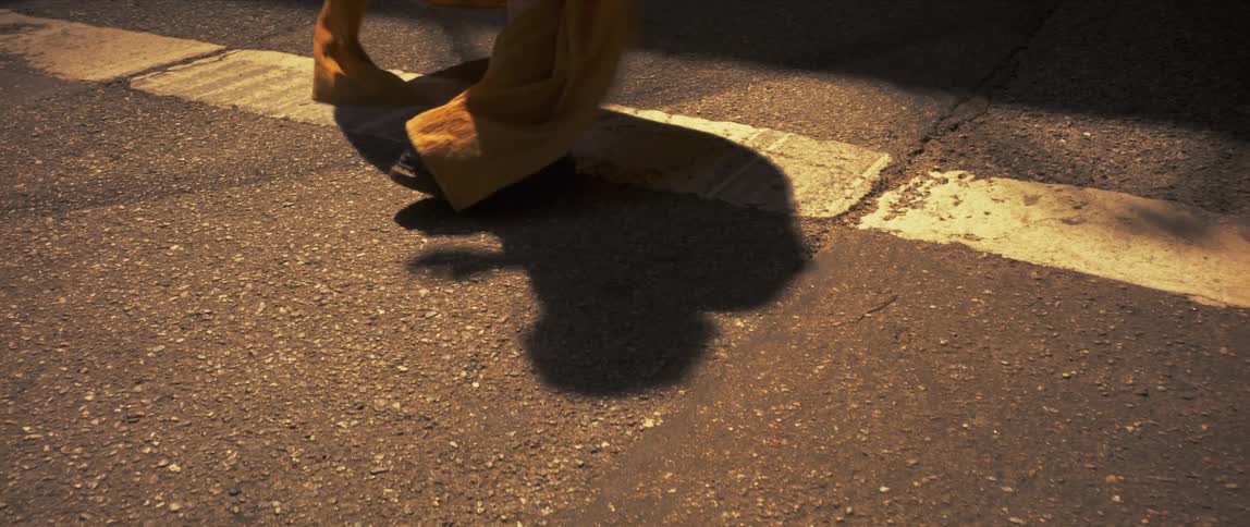 A womens shadow is reflected onto pavement as she dances in combat boots in the middle of a street