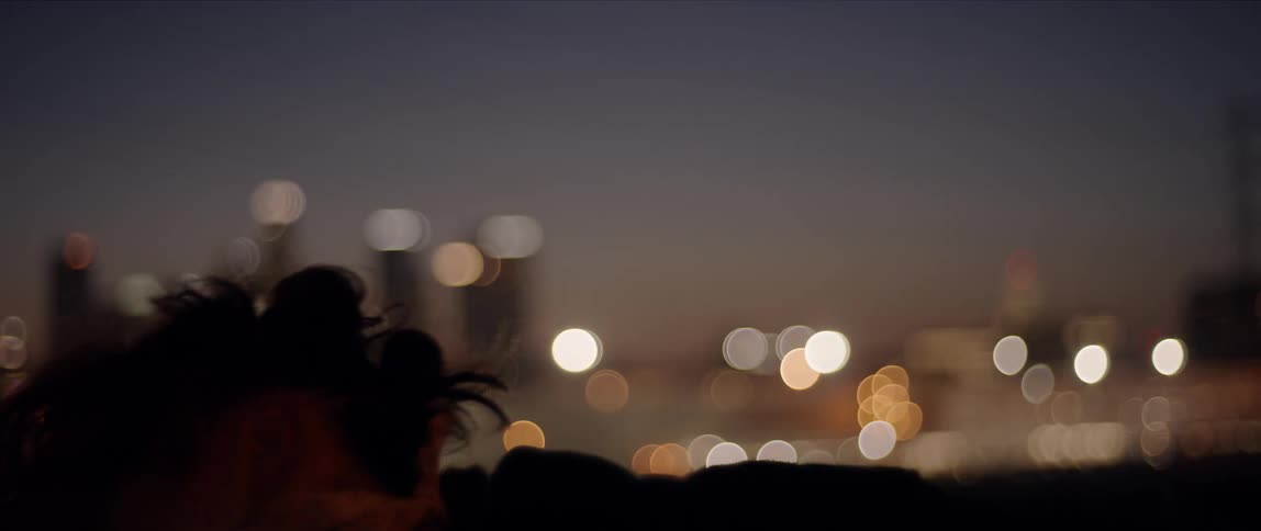 A young woman with a bandana covering her lower face dances outdoors in a metropolis at night