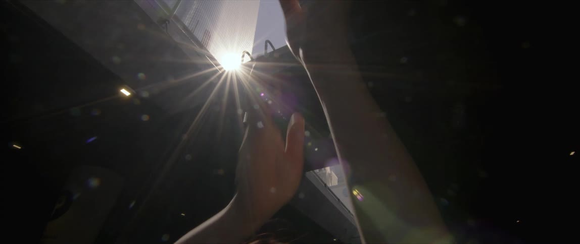 Young woman waving her hands in front of the reflection of the sun on a tall skyscraper in the city