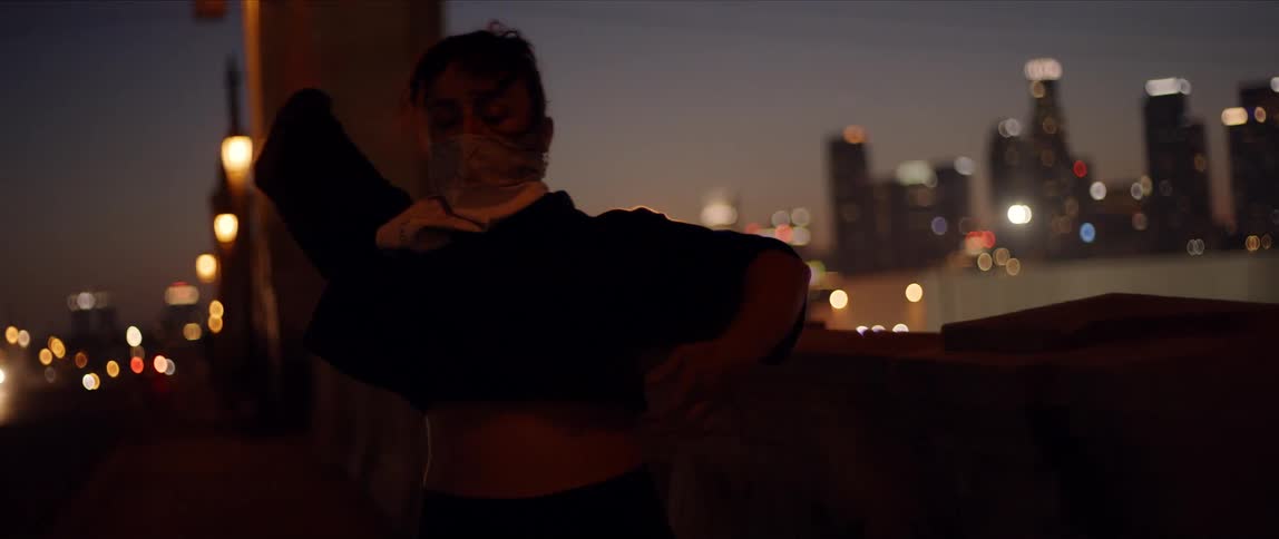 A young woman dances on a bridge in a metropolis at night