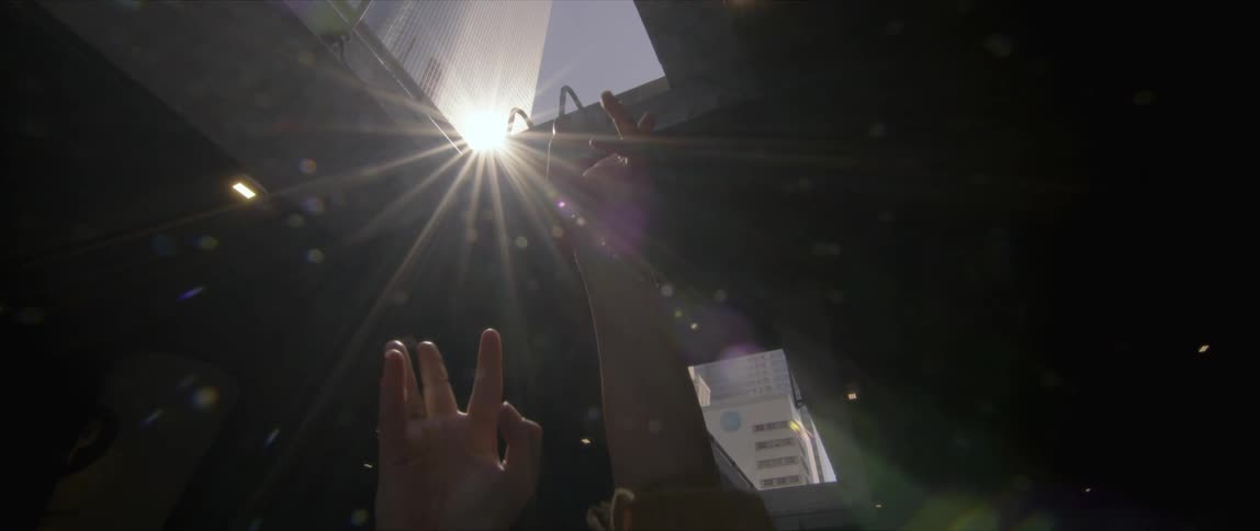 Person dances under under structure in light reflected from high rise and coming through roof opening