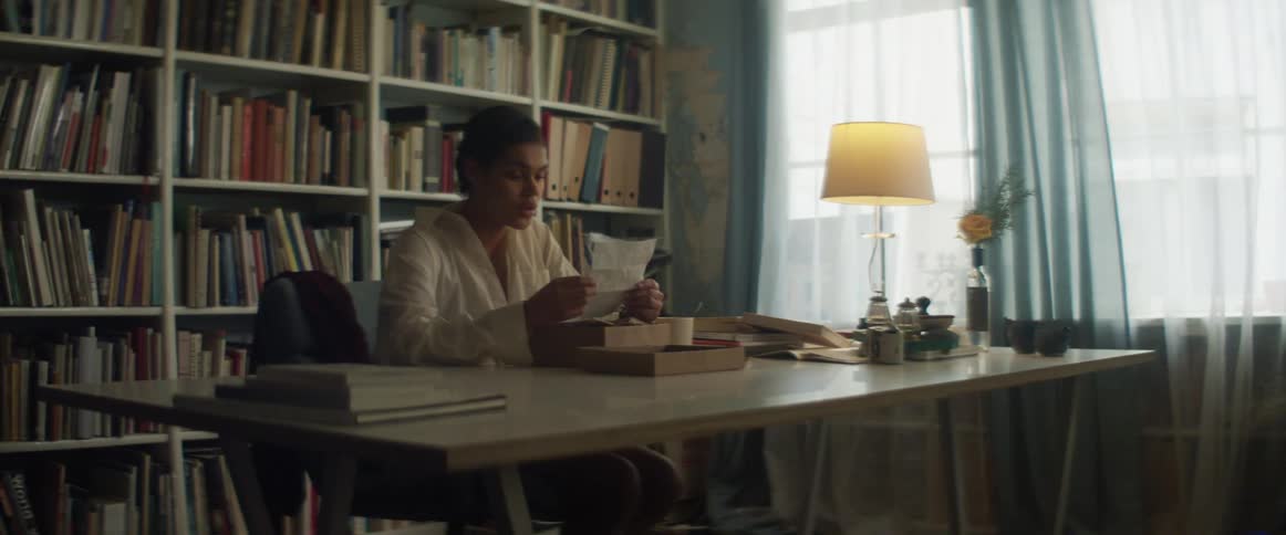 A woman sitting at a desk at home reads a paper